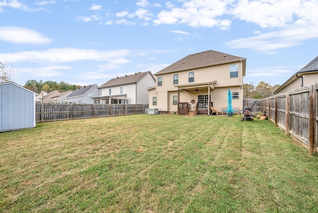 back of house with a yard, central AC unit, a ceiling fan, a fenced backyard, and an outdoor structure