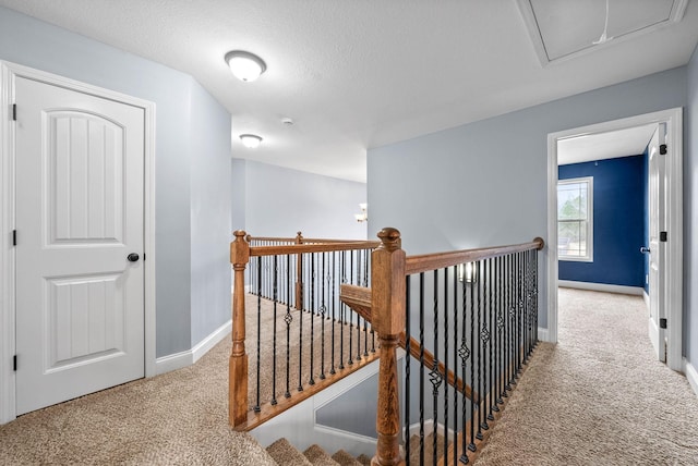 hallway with attic access, carpet, baseboards, and an upstairs landing