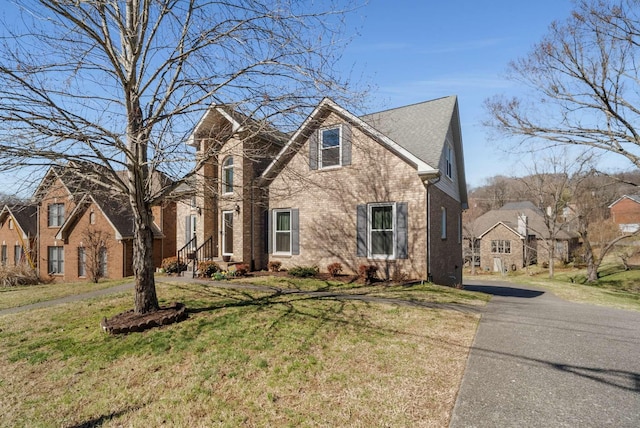 traditional-style home with a shingled roof, a front yard, and brick siding