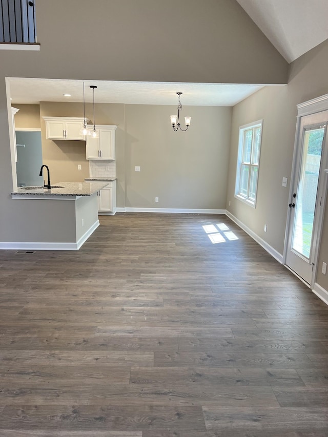 unfurnished living room featuring baseboards, dark wood-style floors, a sink, vaulted ceiling, and a notable chandelier