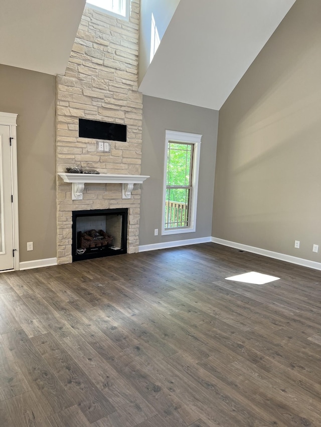 unfurnished living room with a stone fireplace, dark wood finished floors, a towering ceiling, and baseboards