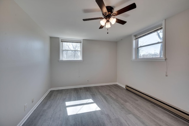 spare room with a baseboard heating unit, ceiling fan, baseboards, and wood finished floors