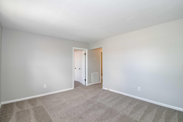 empty room with a textured ceiling, carpet flooring, visible vents, and baseboards