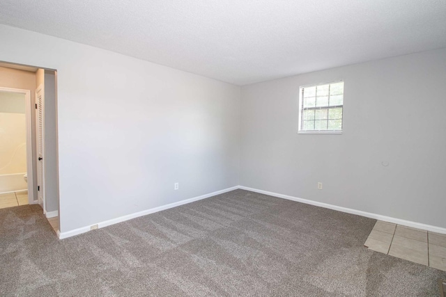 tiled spare room featuring carpet floors, baseboards, and a textured ceiling