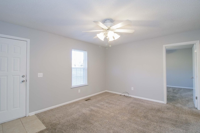 spare room featuring light tile patterned floors, visible vents, ceiling fan, a textured ceiling, and baseboards