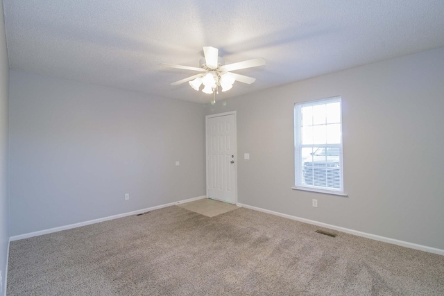 empty room with ceiling fan, a textured ceiling, light carpet, visible vents, and baseboards