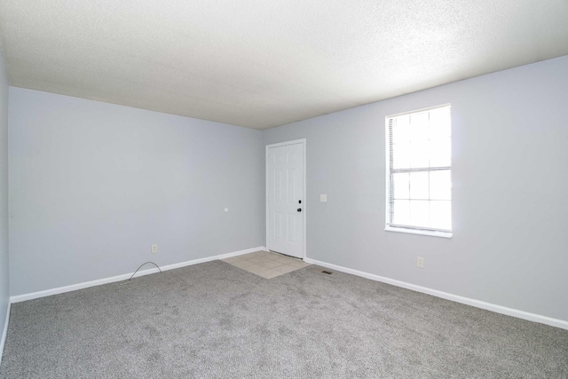 empty room featuring carpet floors, visible vents, a textured ceiling, and baseboards