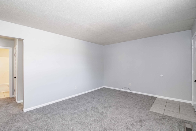 carpeted spare room featuring visible vents, a textured ceiling, baseboards, and tile patterned floors