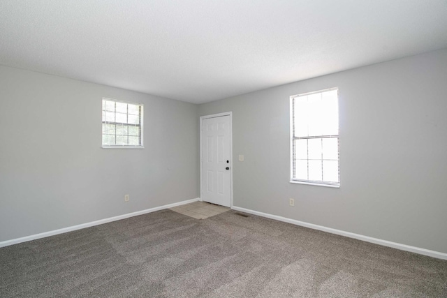 spare room with carpet floors, visible vents, a textured ceiling, and baseboards