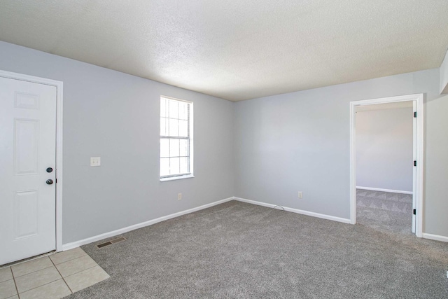 carpeted empty room featuring a textured ceiling, tile patterned floors, visible vents, and baseboards