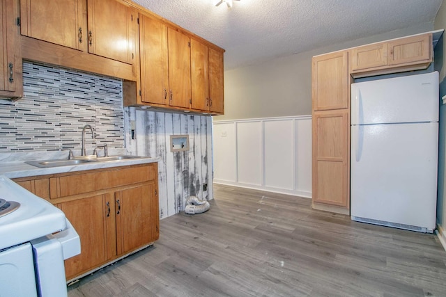 kitchen featuring light countertops, light wood-style flooring, a sink, a textured ceiling, and white appliances