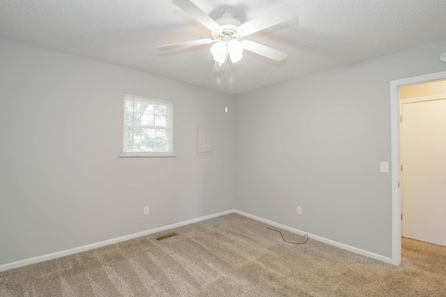 carpeted spare room with ceiling fan, visible vents, baseboards, and a textured ceiling