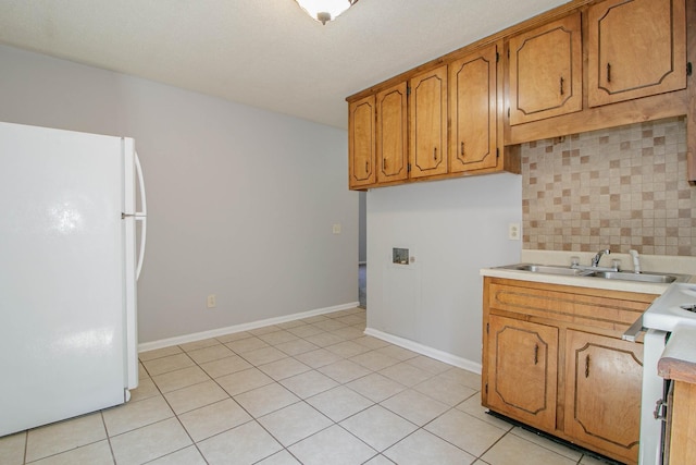 kitchen featuring a sink, light countertops, backsplash, freestanding refrigerator, and brown cabinets