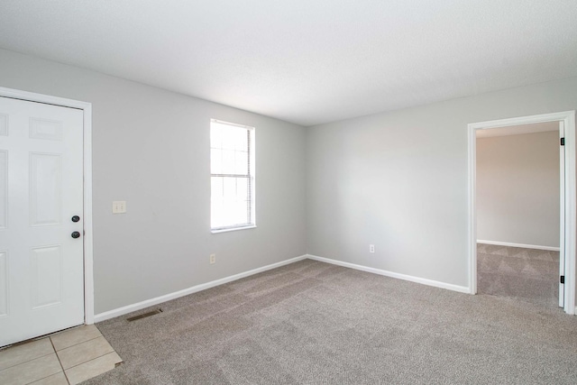 carpeted empty room with tile patterned flooring, visible vents, and baseboards