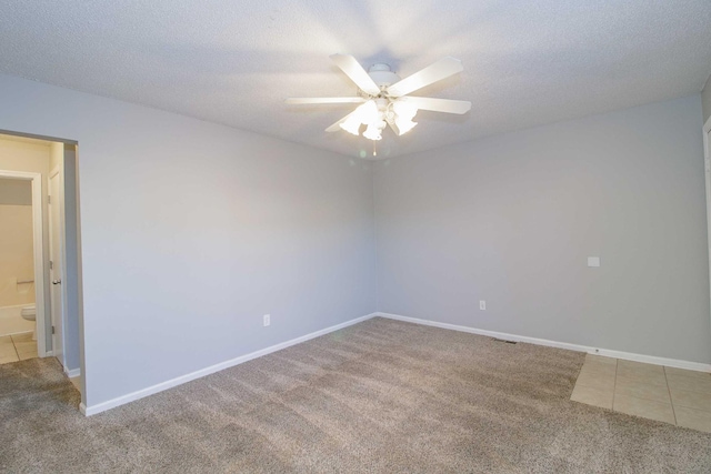 carpeted empty room featuring tile patterned flooring, ceiling fan, baseboards, and a textured ceiling