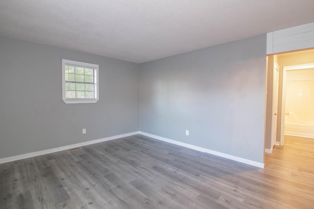 empty room with a textured ceiling, baseboards, and wood finished floors