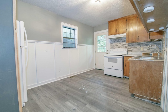 kitchen with light countertops, light wood-style floors, a sink, white appliances, and under cabinet range hood