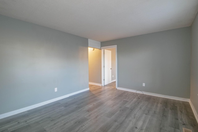 spare room with a textured ceiling, baseboards, and wood finished floors