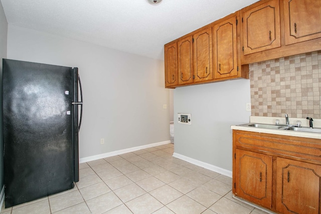 kitchen featuring a sink, light countertops, freestanding refrigerator, decorative backsplash, and brown cabinetry