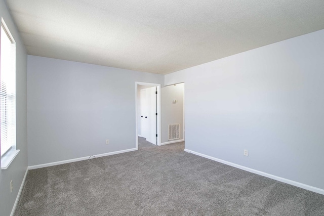 carpeted spare room featuring visible vents, a textured ceiling, and baseboards