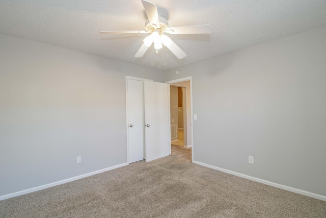 empty room with a textured ceiling, ceiling fan, carpet flooring, and baseboards