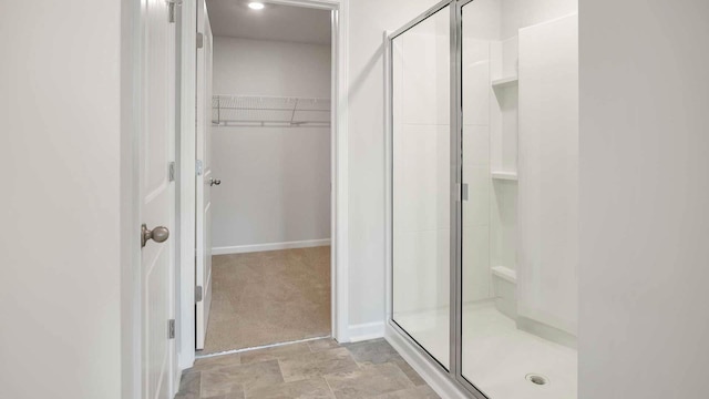 bathroom with a shower stall, a walk in closet, and baseboards