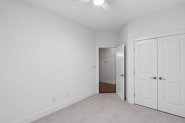 unfurnished bedroom featuring a ceiling fan, a closet, light colored carpet, and baseboards