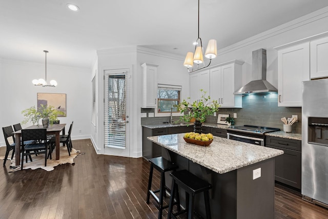 kitchen with wall chimney exhaust hood, dark wood-type flooring, stainless steel appliances, crown molding, and a chandelier