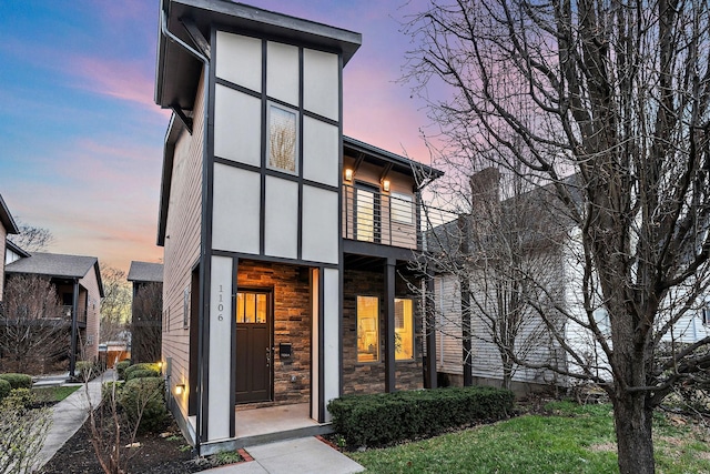 view of front of home with stone siding, a balcony, and stucco siding