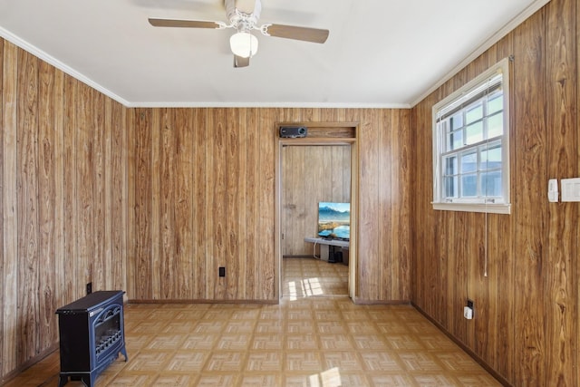 unfurnished room with ceiling fan, wood walls, a wood stove, and baseboards