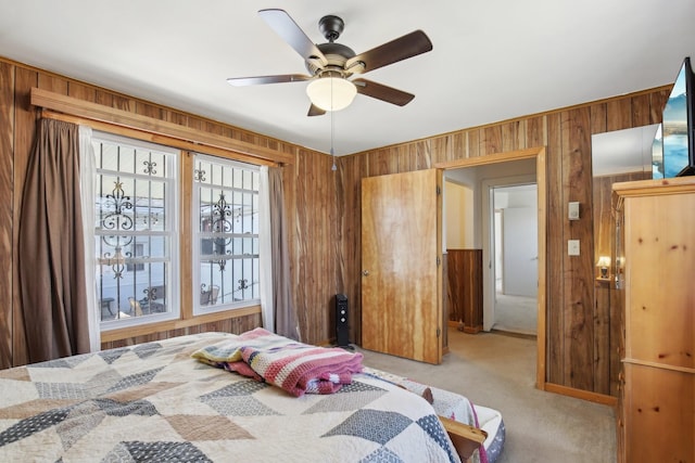 bedroom featuring wooden walls, a ceiling fan, and light colored carpet