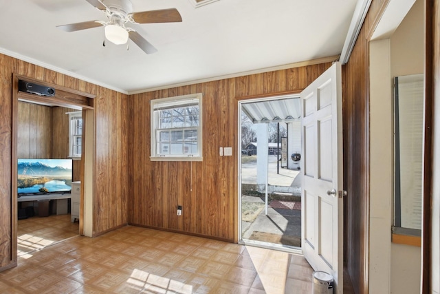 interior space with wood walls, baseboards, and a ceiling fan