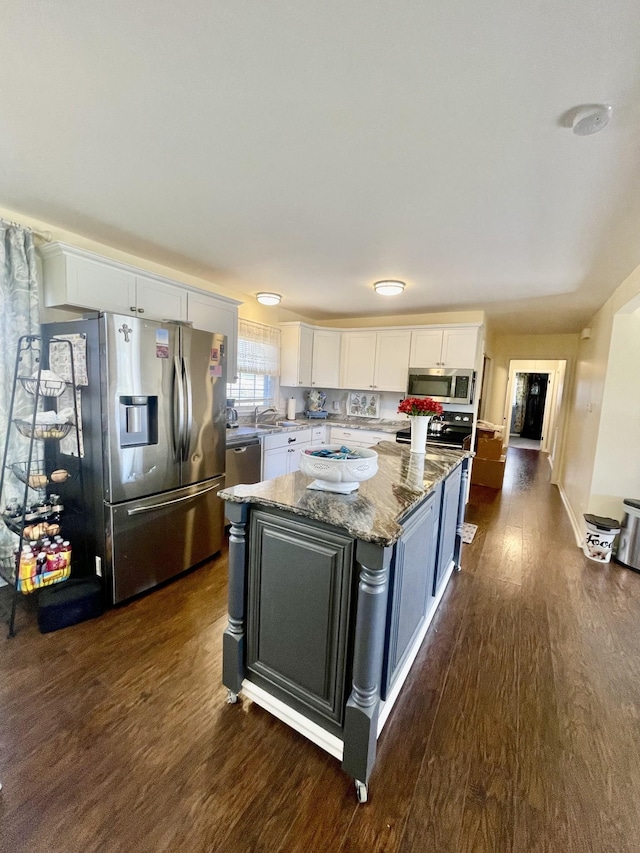 kitchen with light stone countertops, dark wood-style flooring, white cabinets, appliances with stainless steel finishes, and a center island