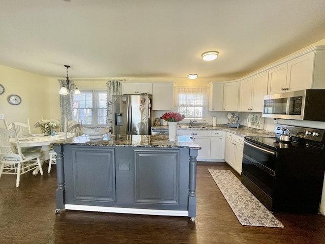 kitchen with stone counters, a sink, a kitchen island, white cabinets, and appliances with stainless steel finishes