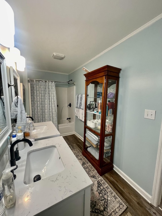 bathroom featuring crown molding, double vanity, a sink, wood finished floors, and baseboards