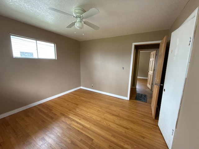 unfurnished bedroom with a ceiling fan, light wood-style flooring, baseboards, and a textured ceiling