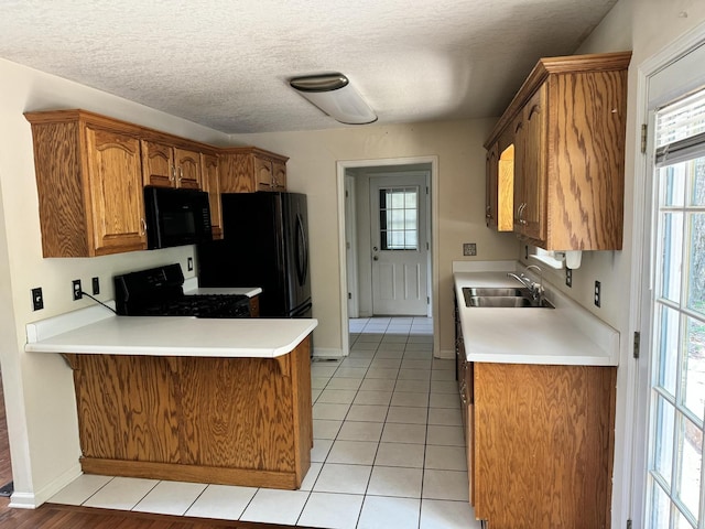 kitchen featuring light tile patterned floors, a peninsula, a sink, light countertops, and black appliances