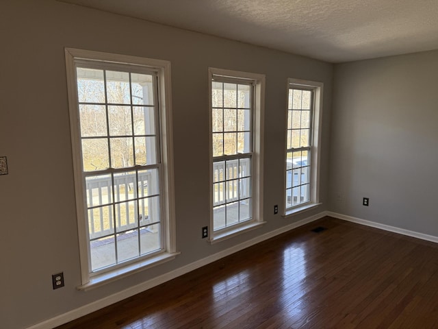 empty room with dark wood-style floors, visible vents, a textured ceiling, and baseboards