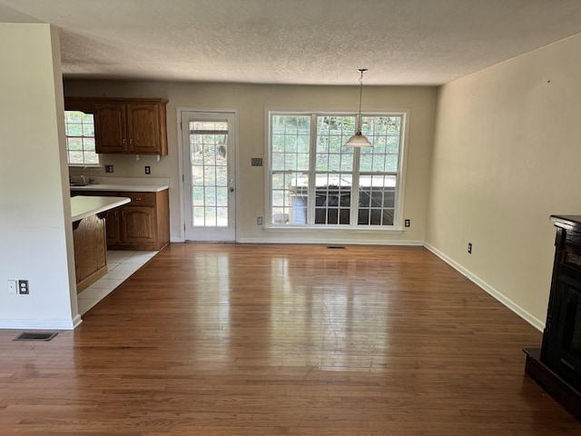 unfurnished dining area with light wood finished floors, visible vents, a sink, a textured ceiling, and baseboards