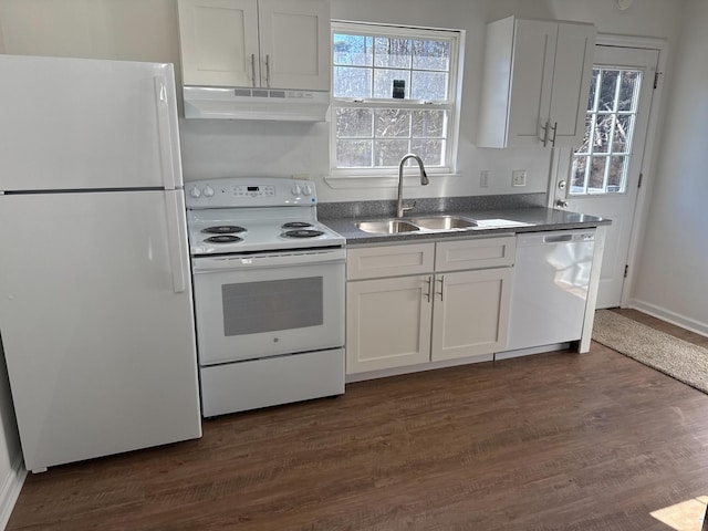 kitchen featuring white appliances, dark countertops, dark wood-type flooring, under cabinet range hood, and a sink