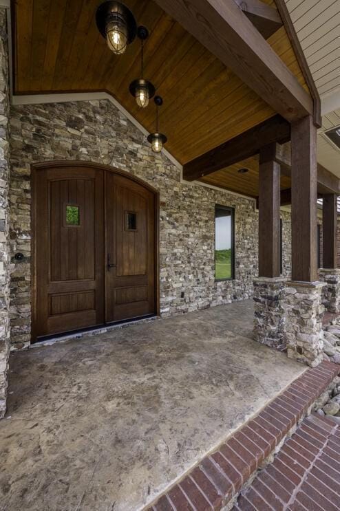 view of exterior entry with stone siding and a patio