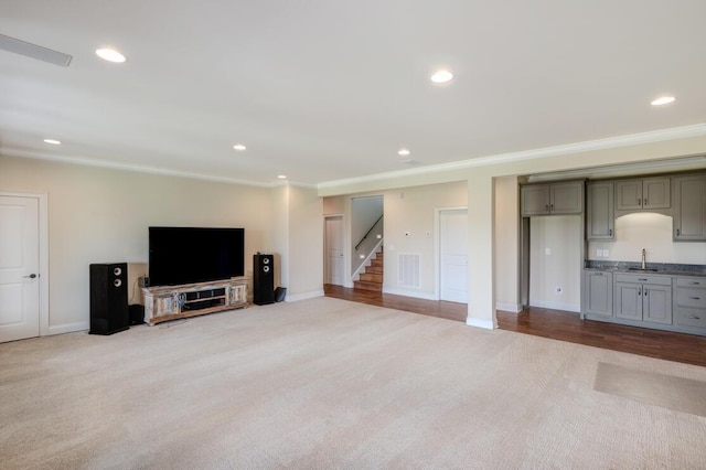 carpeted living area featuring baseboards, stairs, crown molding, a sink, and recessed lighting