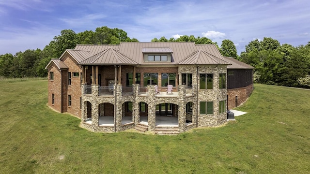 rear view of property with brick siding, a lawn, a standing seam roof, a patio area, and a balcony