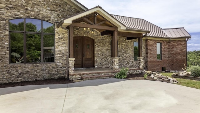 property entrance featuring metal roof, brick siding, a standing seam roof, and stone siding