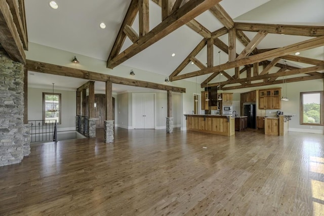 unfurnished living room featuring beam ceiling, high vaulted ceiling, wood finished floors, a chandelier, and baseboards