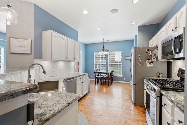 kitchen featuring light stone counters, stainless steel appliances, a sink, light wood-style floors, and white cabinets