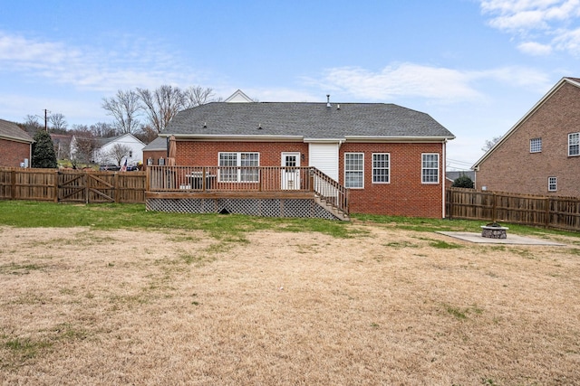 rear view of house with a fire pit, a lawn, a fenced backyard, a deck, and brick siding