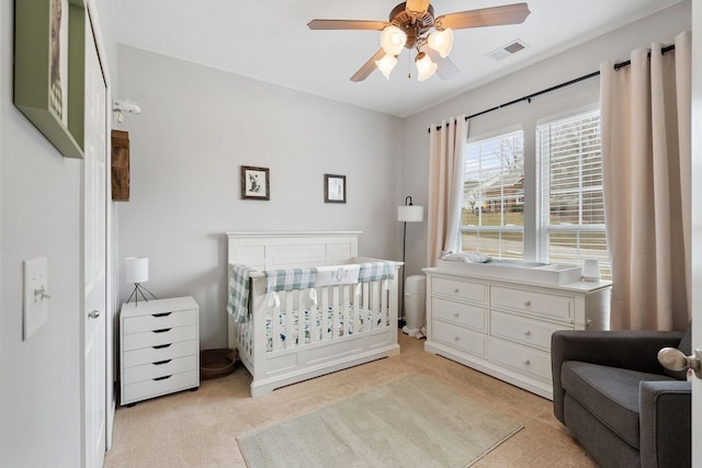 bedroom with light carpet, visible vents, ceiling fan, and a crib