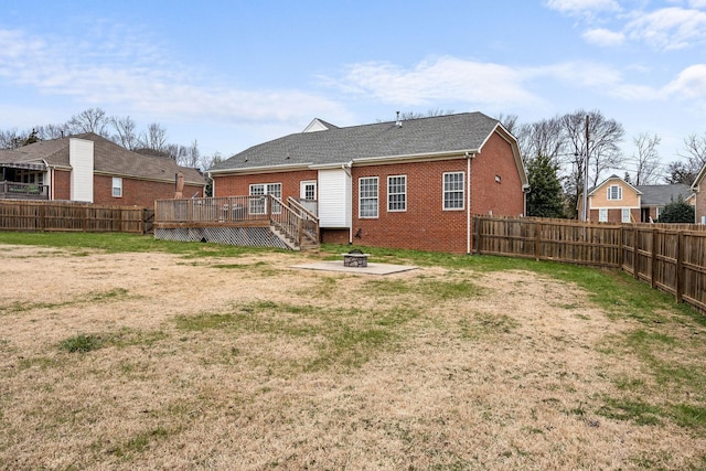 rear view of property with a fenced backyard, a fire pit, brick siding, a lawn, and a wooden deck