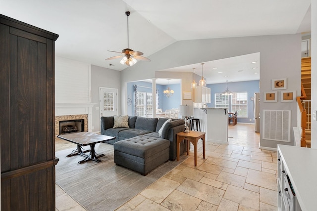 living room featuring a fireplace, lofted ceiling, stone tile flooring, visible vents, and ceiling fan with notable chandelier